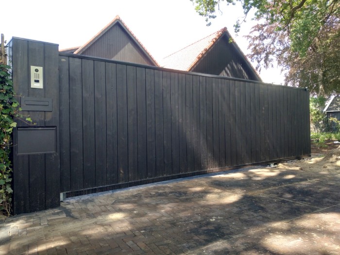 Een houten schuifpoort biedt privacy en bespaart ruimte Een donkerbruine houten schuifpoort schermt een woonerf af.